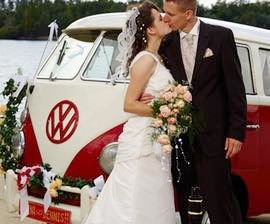 Ein Brautpaar küsst sich vor dem geschmückten VW Hochzeitsbulli während der Fotosession